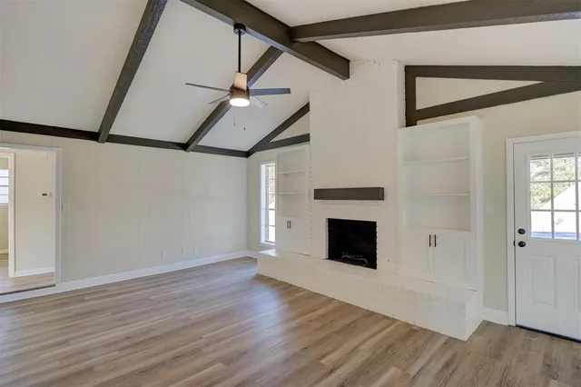 a view of an empty room with wooden floor fireplace and a window