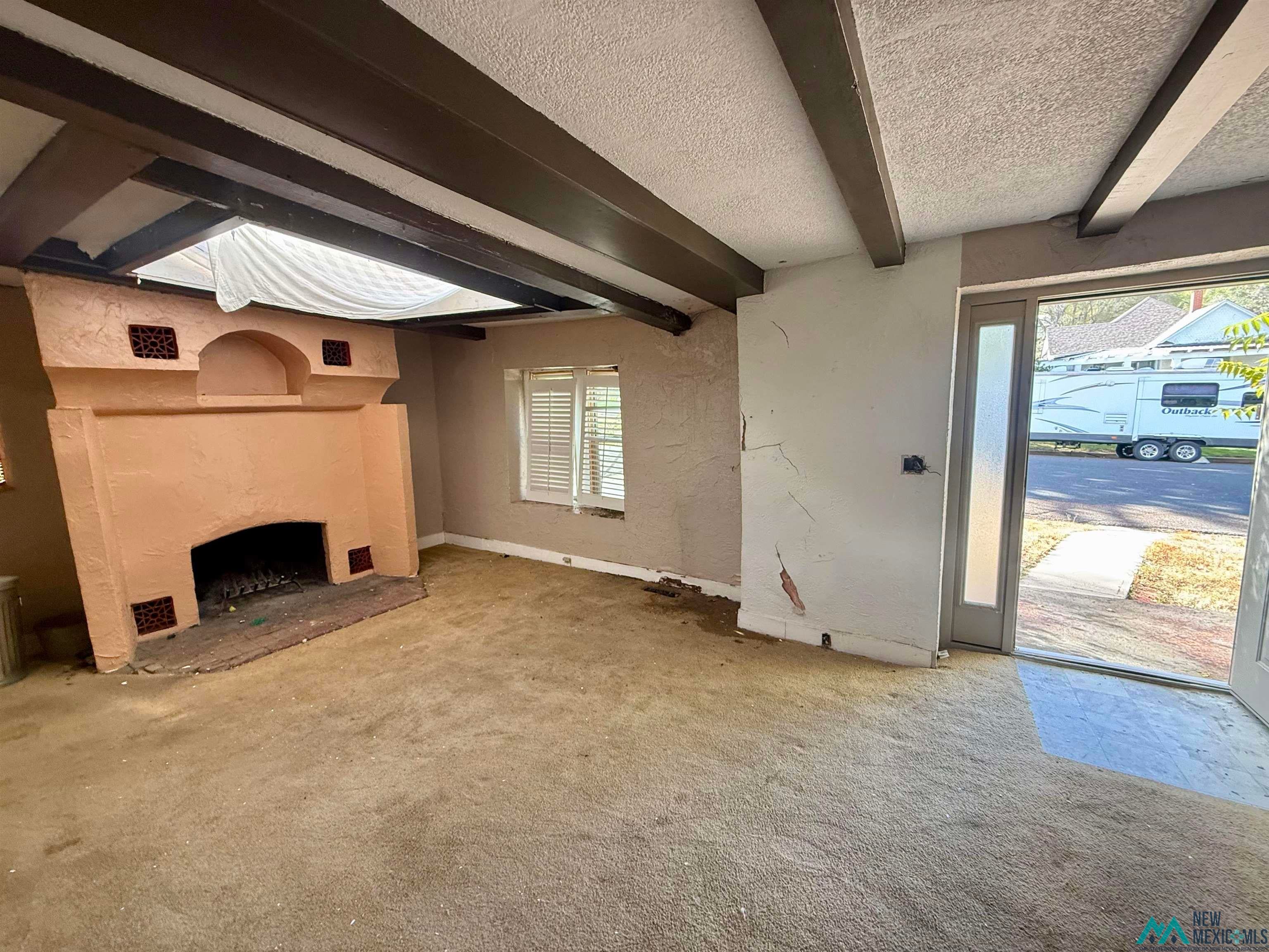 625 South 5th Street Raton, NM 87740 - Photo 14 of 45 Unfurnished living room with beamed ceiling, a textured ceiling, a fireplace, carpet flooring, and a textured wall