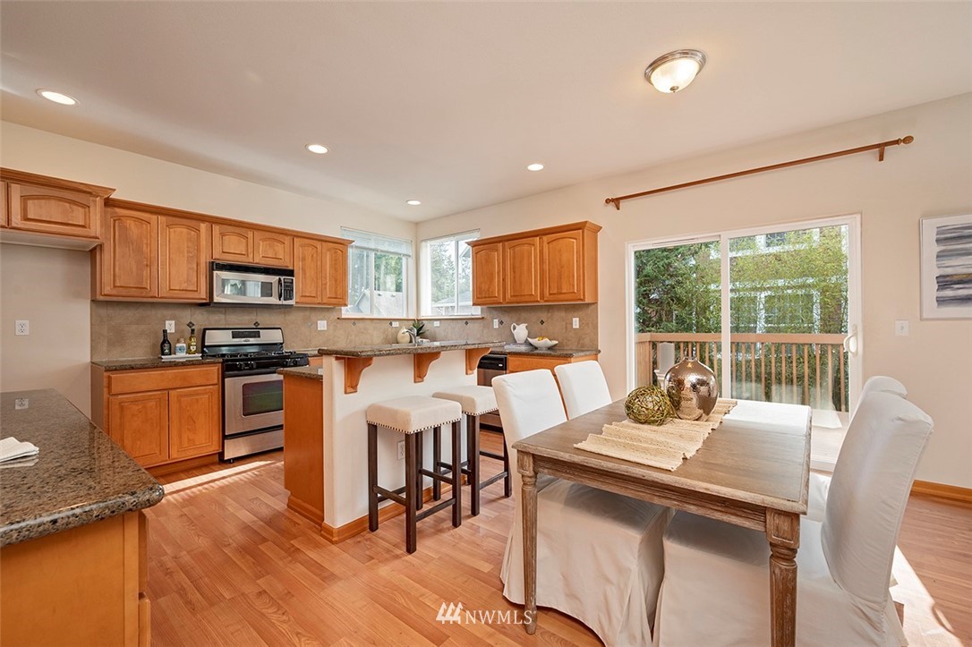 2114 241st Street Southwest Bothell, WA 98021 - Photo 8 of 32 a kitchen with stainless steel appliances granite countertop a stove top oven a sink dishwasher a dining table and chairs with wooden floor