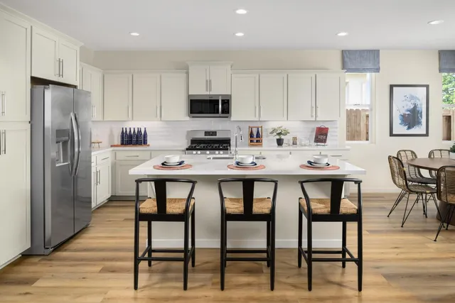 a kitchen with stainless steel appliances granite countertop a dining table chairs refrigerator and microwave