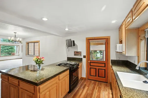 a kitchen with granite countertop a stove a sink dishwasher and a dining table with wooden floor