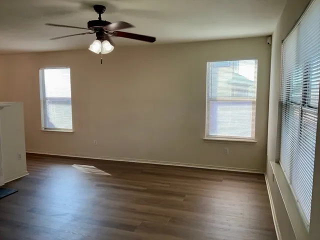 an empty room with wooden floor fan and windows
