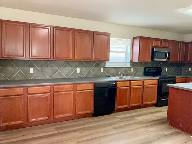 a kitchen with stainless steel appliances granite countertop wooden cabinets a stove top oven a sink and dishwasher with wooden floor