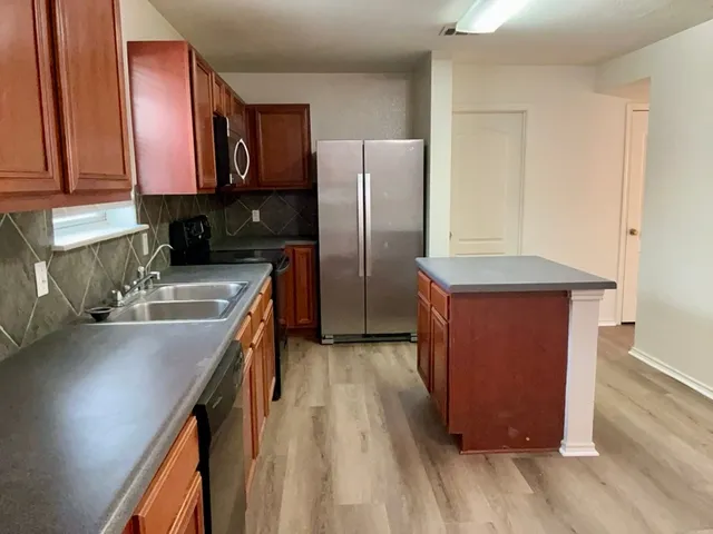 a kitchen with stainless steel appliances granite countertop a refrigerator a sink dishwasher a stove and a microwave oven with wooden floor