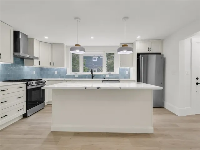 a large kitchen with stainless steel appliances a large counter top a stove a refrigerator and a sink