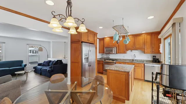 a kitchen with stainless steel appliances granite countertop a stove a refrigerator a sink dishwasher a dining table and chairs with wooden floor