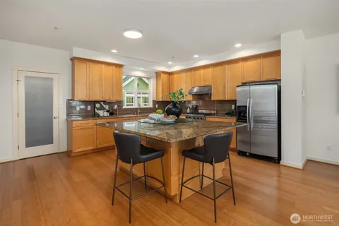 a kitchen with stainless steel appliances granite countertop a stove a refrigerator a sink a dining table and chairs with wooden floor