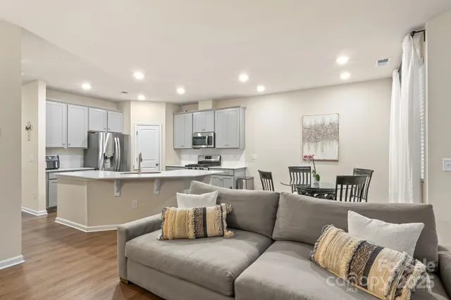 a living room with white couches and kitchen view with wooden floor
