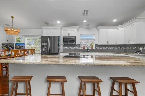 a kitchen with stainless steel appliances granite countertop a sink a stove a refrigerator cabinets and chairs