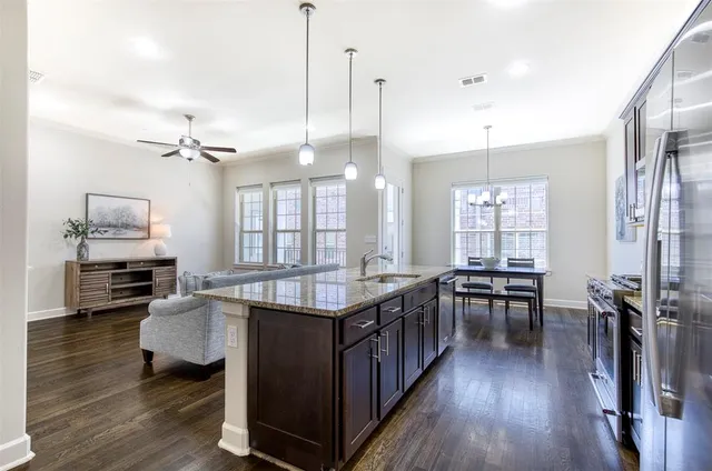 a kitchen with stainless steel appliances granite countertop a stove top oven a refrigerator a dining table and chairs with wooden floor