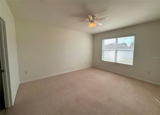 an empty room with a chandelier fan and windows