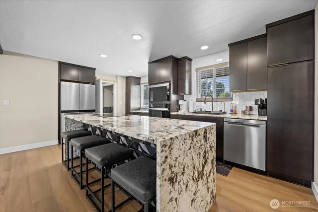 a kitchen with stainless steel appliances kitchen island granite countertop a refrigerator a stove a sink a dining table and chairs with wooden floor