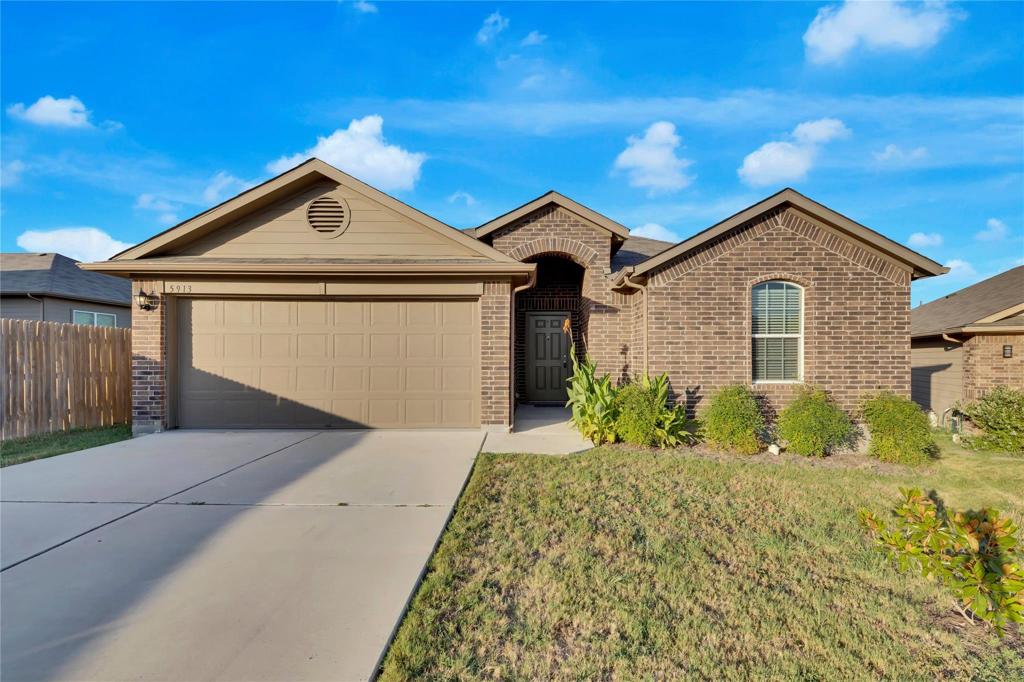 Brick-front home featuring an arched entry, an attached garage with a tan door, and a concrete driveway
