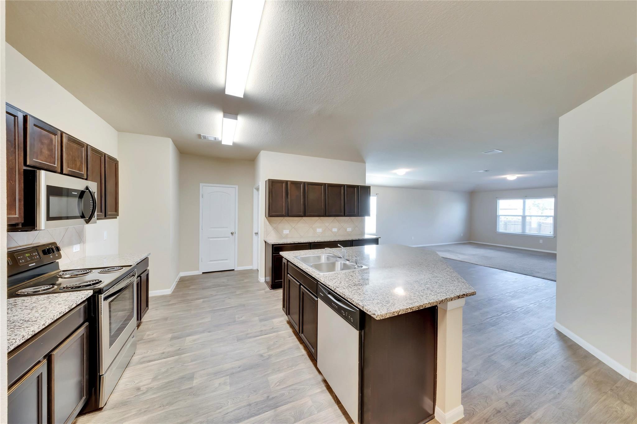5913 Diamondleaf Bend Austin, TX 78724 - Photo 2 of 20 Kitchen featuring wood-finish flooring, dark wood cabinetry, light speckled countertops, stainless steel appliances, and a central island with an integrated sink