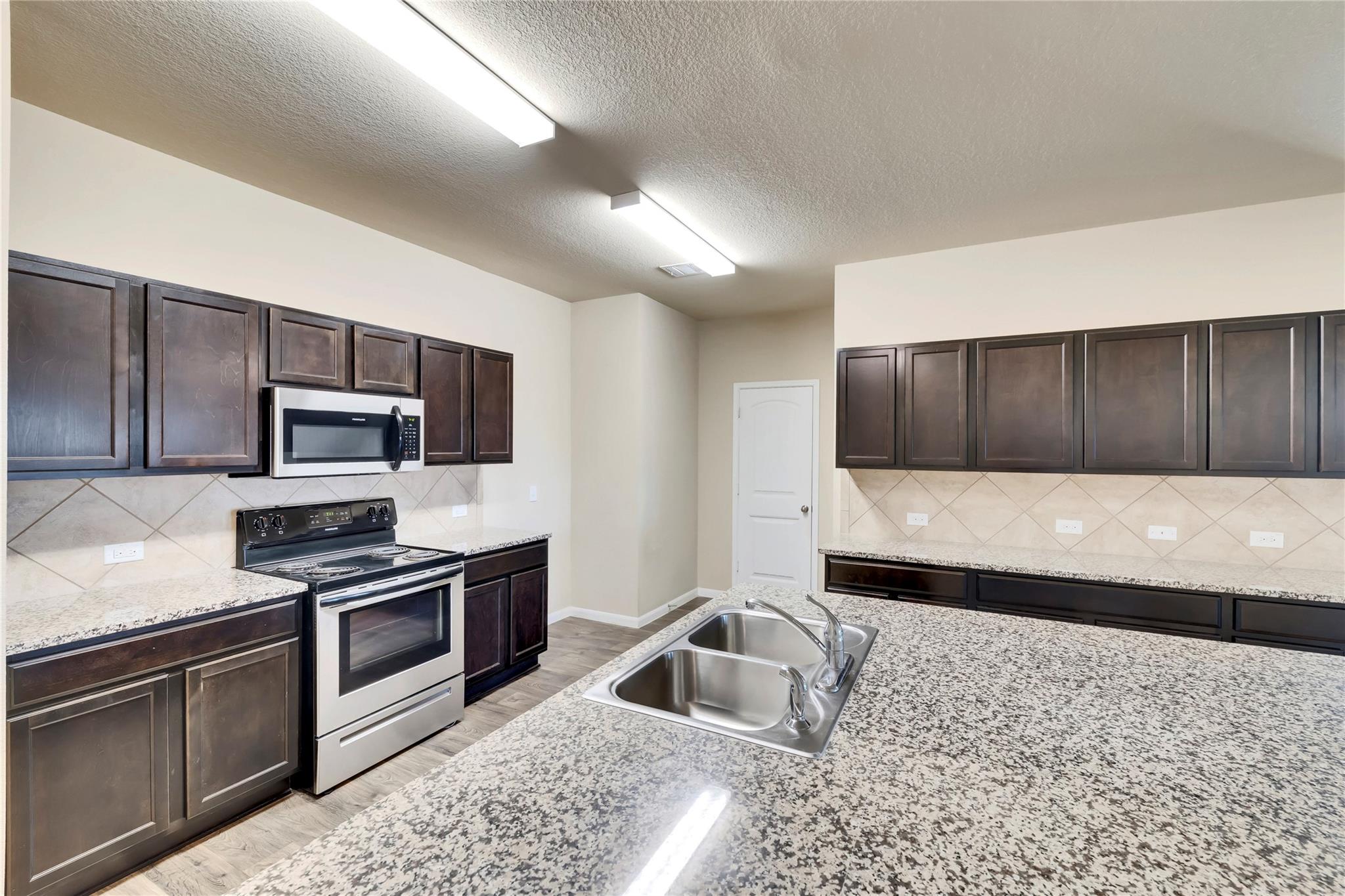 5913 Diamondleaf Bend Austin, TX 78724 - Photo 3 of 20 Kitchen featuring extensive granite countertops, stainless steel appliances, dark wood-finish cabinetry, and a dual basin sink