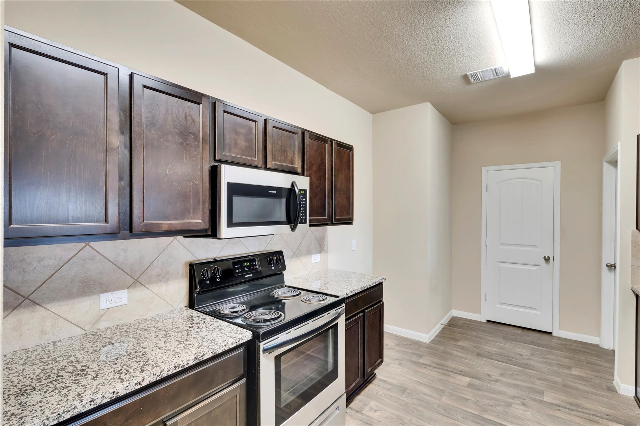 5913 Diamondleaf Bend Austin, TX 78724 - Photo 4 of 20 Kitchen featuring wood-finish flooring, dark wood cabinetry, light-toned granite-style countertops, a stainless steel electric range, and a built-in microwave