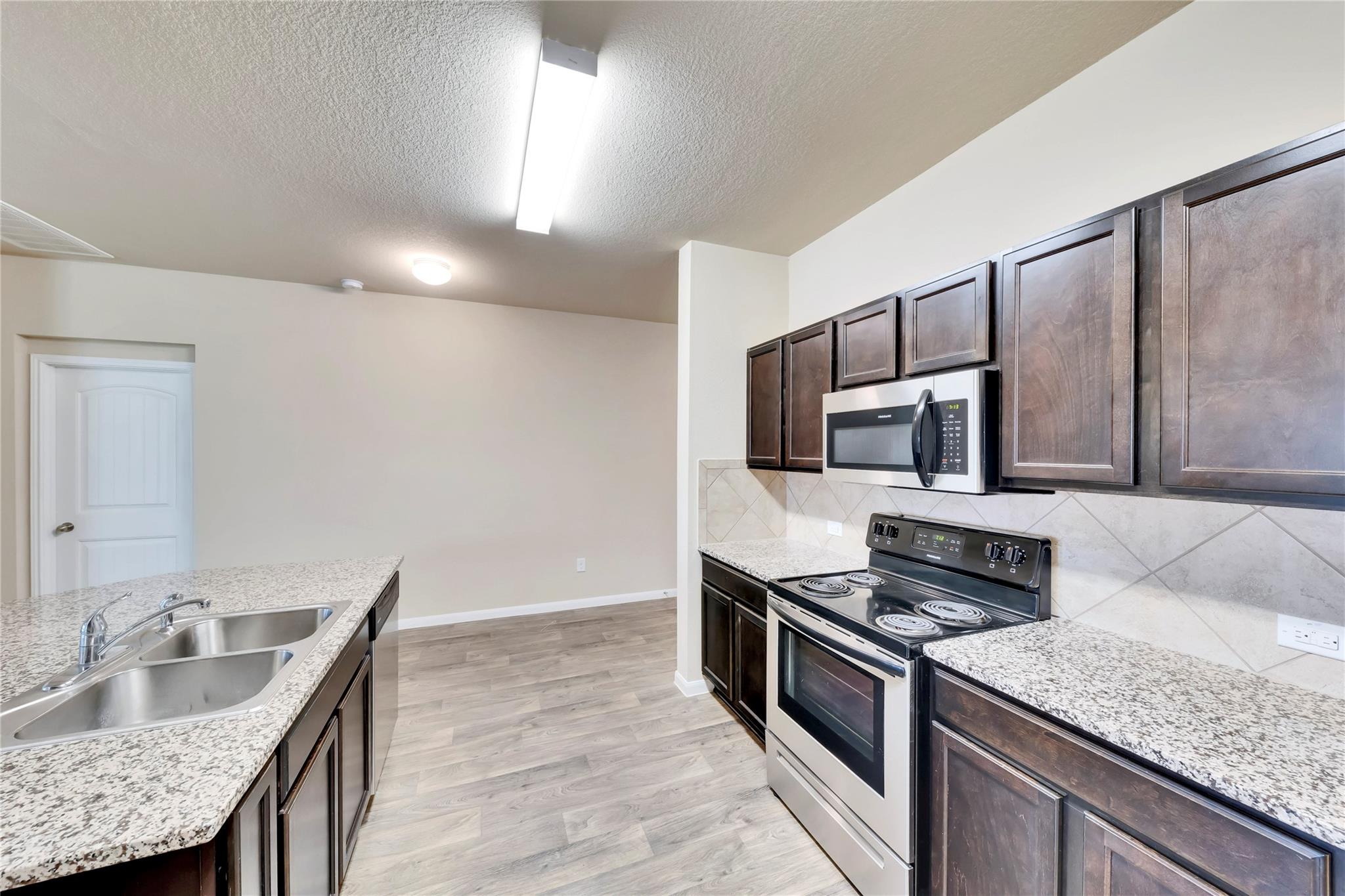 5913 Diamondleaf Bend Austin, TX 78724 - Photo 5 of 20 Kitchen featuring stainless steel appliances, dark wood-finish cabinetry, granite-style countertops, and a tile backsplash