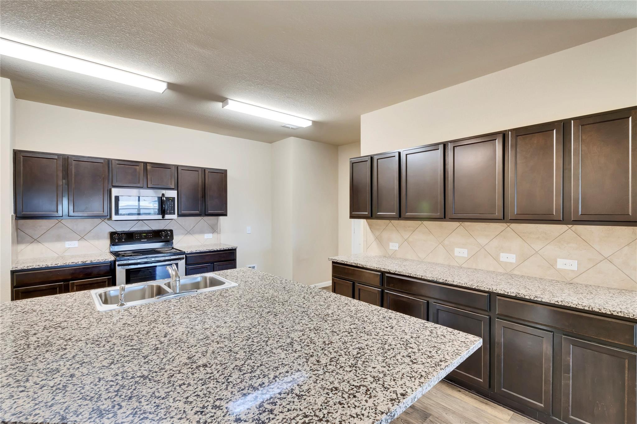 5913 Diamondleaf Bend Austin, TX 78724 - Photo 6 of 20 Kitchen featuring dark wood-finish cabinetry, speckled countertops, stainless steel appliances, and a tile backsplash
