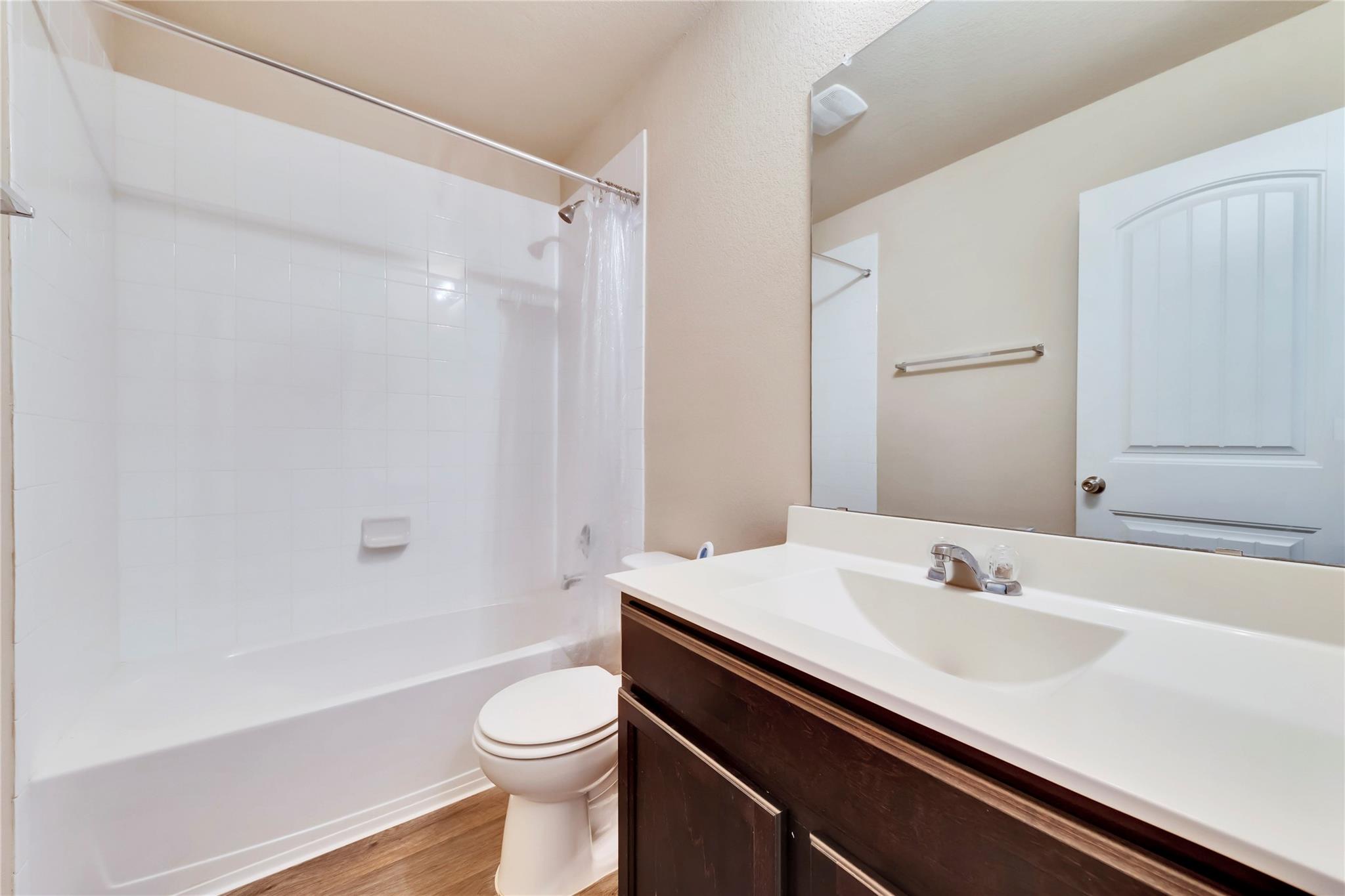 5913 Diamondleaf Bend Austin, TX 78724 - Photo 8 of 20 Bathroom featuring a white bathtub and shower with white tile surround, wood-finish flooring, a white toilet, and a vanity with a white countertop and dark wood-finish cabinetry