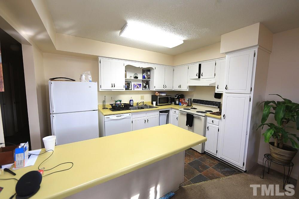 524 Pine Ridge Place, Unit 524 Raleigh, NC 27609 - Photo 6 of 12 a kitchen with a refrigerator a stove a sink dishwasher and white cabinets with wooden floor