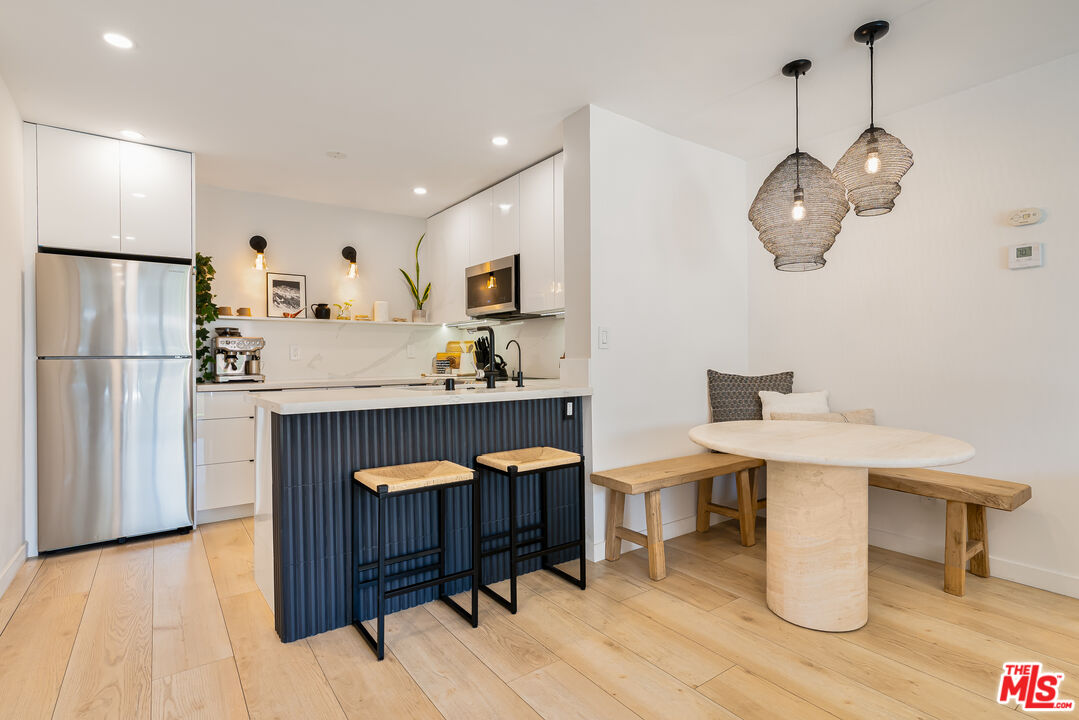 11750 Sunset Boulevard, Unit 407 Los Angeles, CA 90049 - Photo 3 of 12 a kitchen with stainless steel appliances kitchen island a table chairs in it and wooden floors