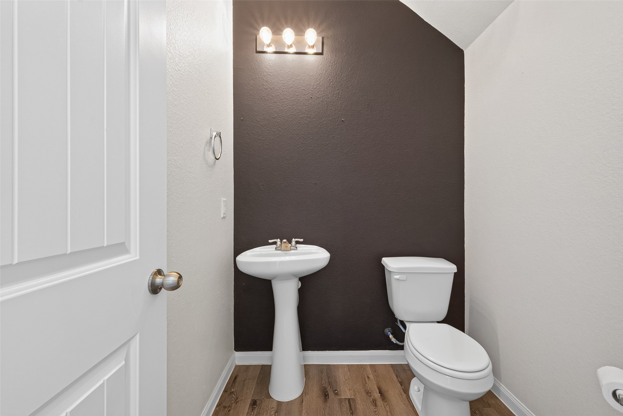 2526 Sturgeon Way Conroe, TX 77384 - Photo 17 of 49 This is a compact half-bathroom featuring a pedestal sink and toilet. It has a dark accent wall, modern light fixture, and wood-style flooring, creating a clean and simple look.