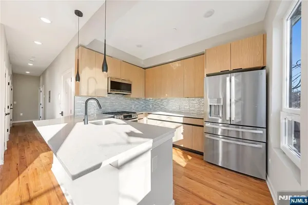 a kitchen with stainless steel appliances granite countertop a sink a stove a refrigerator and island with wooden floor