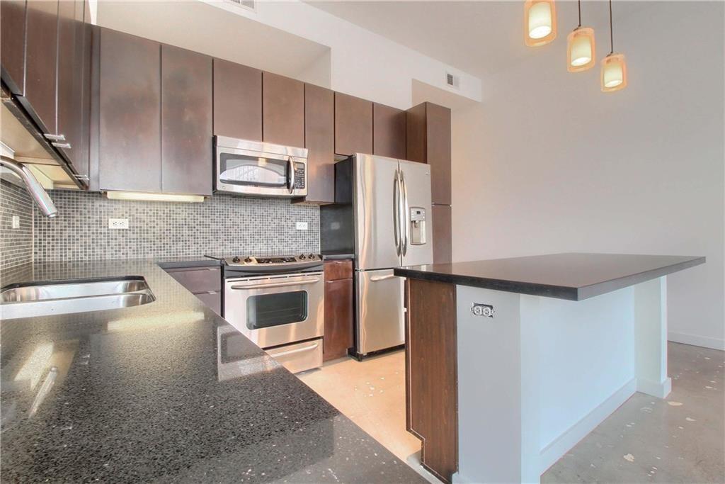507 Sabine Street, Unit 602 Austin, TX 78701 - Photo 2 of 22 a kitchen with granite countertop a refrigerator a stove top oven and a sink with granite countertops