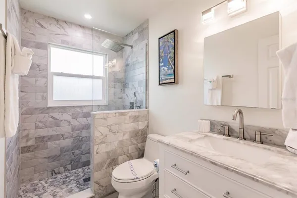 a bathroom with a granite countertop sink a toilet a mirror and shower