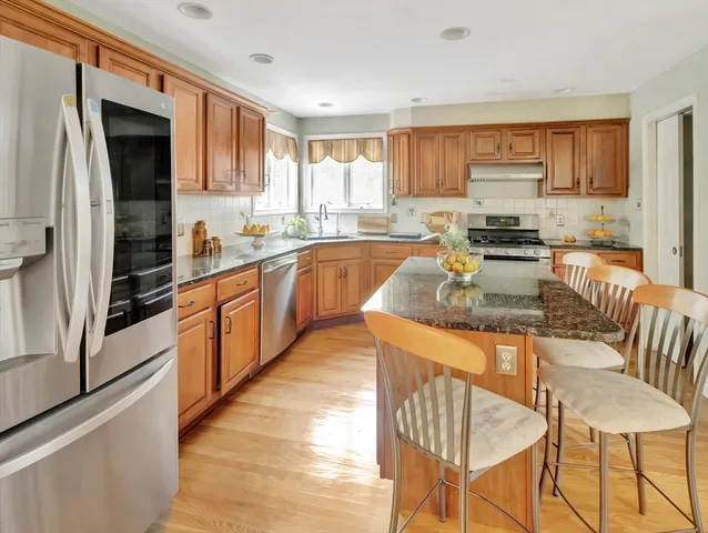 a kitchen with stainless steel appliances granite countertop a stove top oven a sink dishwasher a dining table and chairs with wooden floor