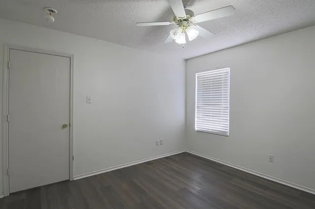 an empty room with wooden floor fan and windows