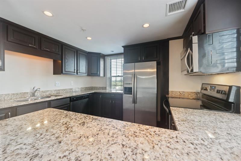 199 14th Street Northeast, Unit 705 Atlanta, GA 30309 - Photo 7 of 20 a kitchen with stainless steel appliances kitchen island granite countertop a refrigerator a sink a stove with wooden cabinets