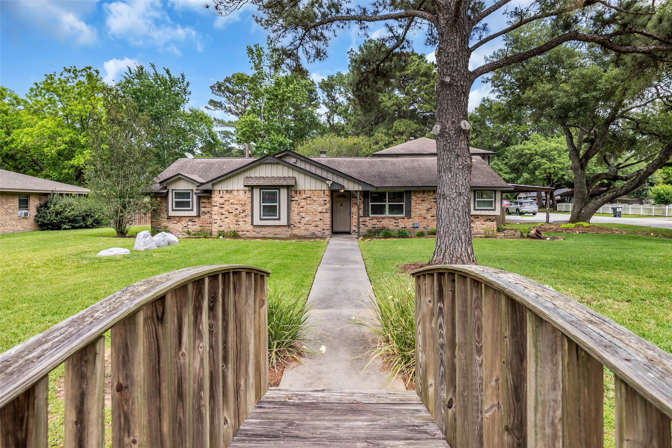 Charming brick home with a welcoming pathway, surrounded by lush greenery and mature trees.