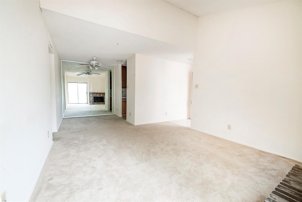 7900 North Stadium Drive, Unit 22 Houston, TX 77030 - Photo 11 of 12 This photo shows a spacious, bright room with light-colored carpet and walls, featuring a ceiling fan and a view into an adjoining room with sliding glass doors leading to the outside.