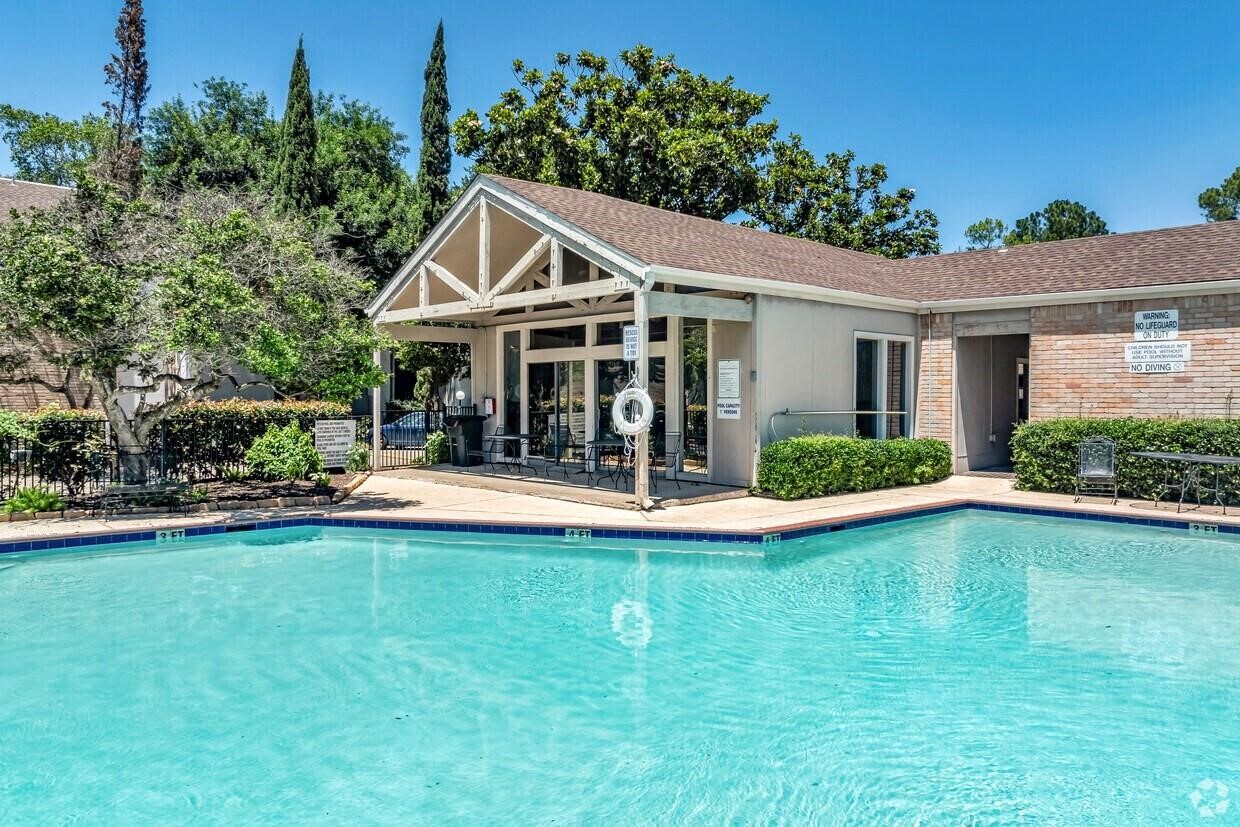 7900 North Stadium Drive, Unit 22 Houston, TX 77030 - Photo 12 of 12 This photo showcases a serene residential pool area with clear blue water, surrounded by a well-maintained clubhouse. The setting is complemented by lush greenery and ample seating, ideal for relaxation and social gatherings.