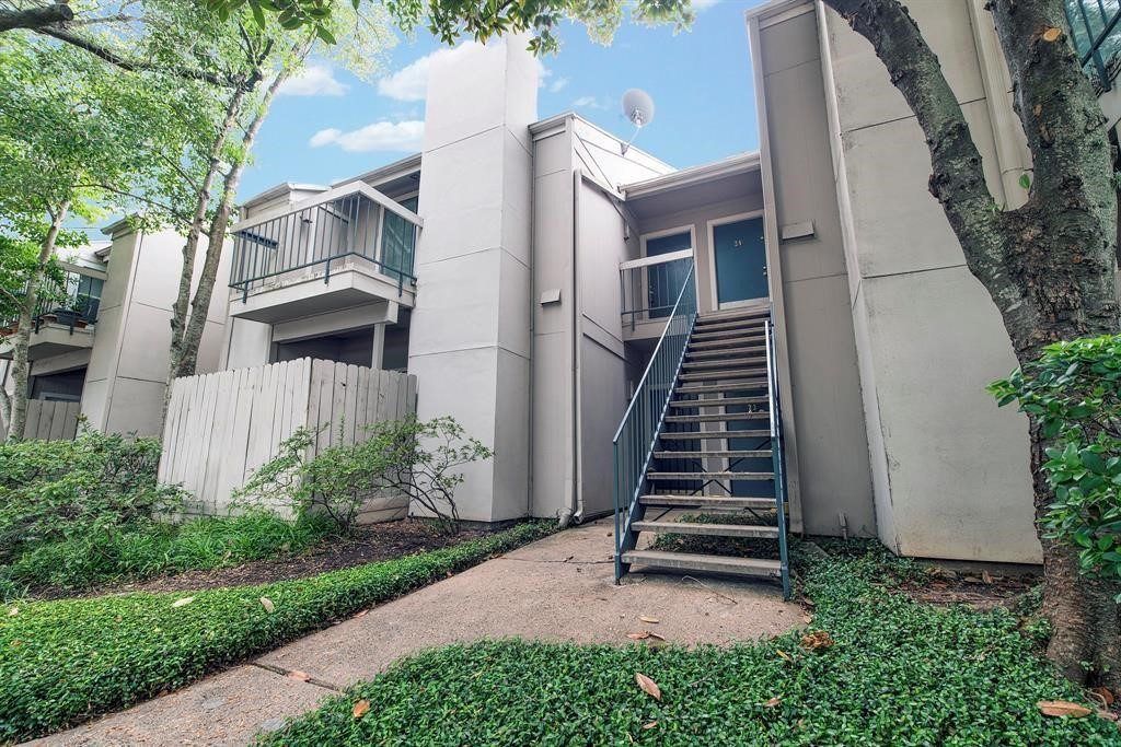 7900 North Stadium Drive, Unit 22 Houston, TX 77030 - Photo 2 of 12 This photo shows a modern, multi-level townhouse with a neutral exterior. It features a staircase leading to the front door, and there are small balconies on the upper levels. The surrounding area is landscaped with greenery, providing a peaceful, natural setting.