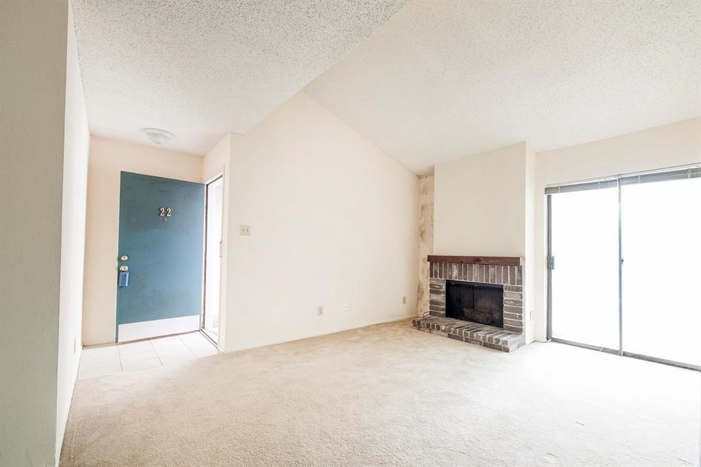 7900 North Stadium Drive, Unit 22 Houston, TX 77030 - Photo 7 of 12 Bright and inviting living room with high ceilings, a cozy brick fireplace, and access to a sliding glass door leading outside. Neutral carpeted flooring complements the space.