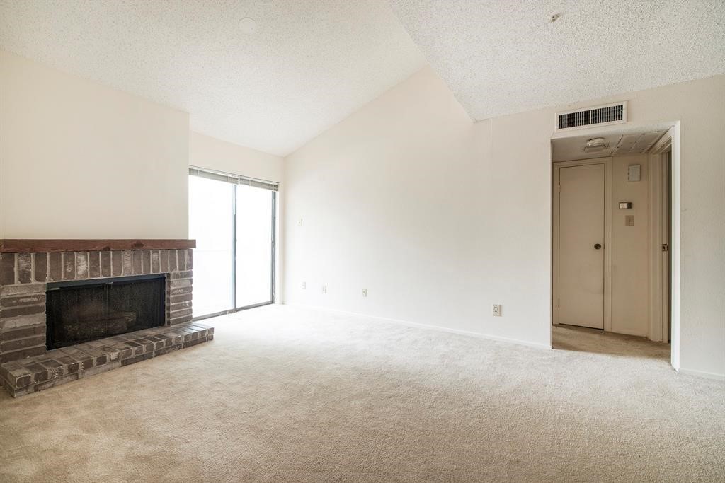 7900 North Stadium Drive, Unit 22 Houston, TX 77030 - Photo 8 of 12 This inviting living room features a cozy brick fireplace, soft carpeting, and ample natural light from a sliding glass door, offering a warm and welcoming atmosphere.