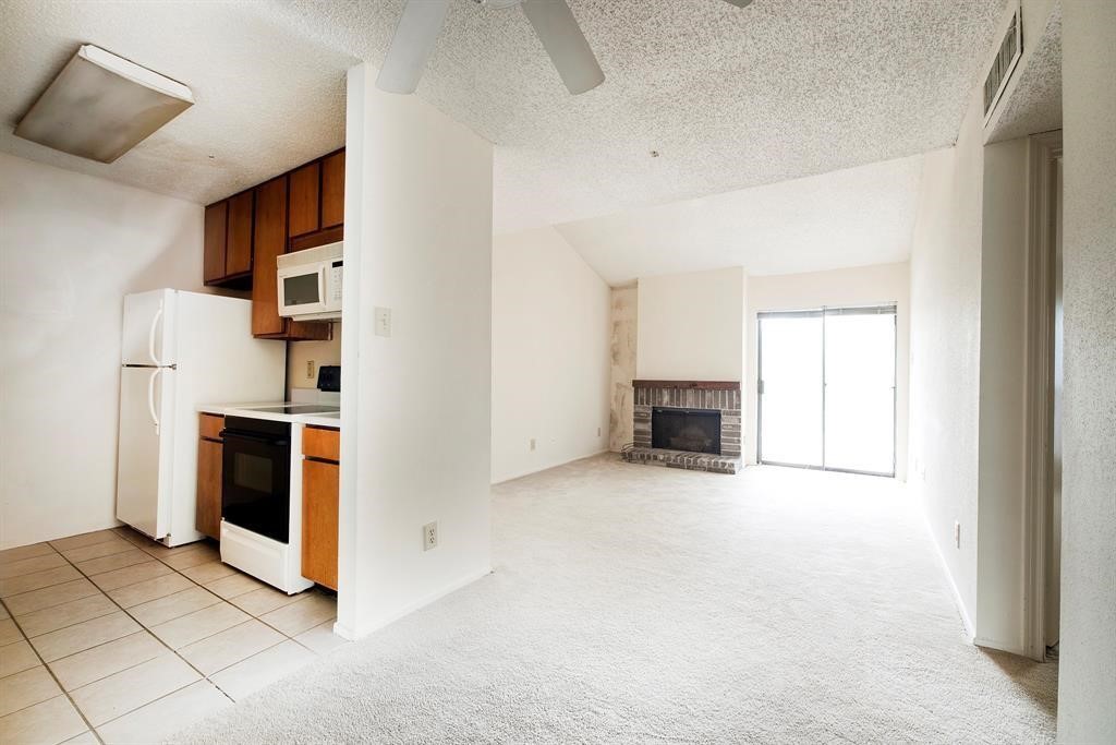7900 North Stadium Drive, Unit 22 Houston, TX 77030 - Photo 9 of 12 This photo shows a cozy living space with an open layout. The kitchen features wood cabinets and modern appliances, while the carpeted living area includes a brick fireplace and sliding glass doors for natural light.