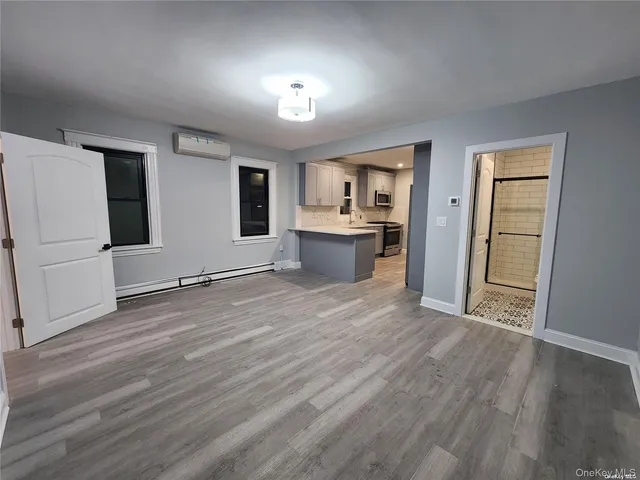 an empty room with wooden floor and kitchen view