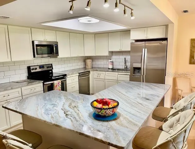 a kitchen with stainless steel appliances kitchen island granite countertop a sink dishwasher stove and refrigerator