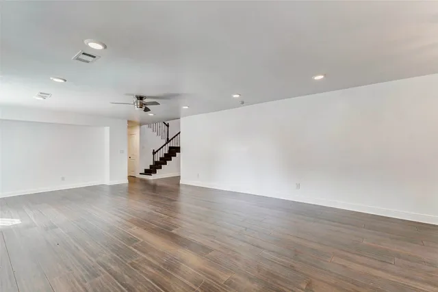 a view of an empty room with wooden floor ceiling fan and windows