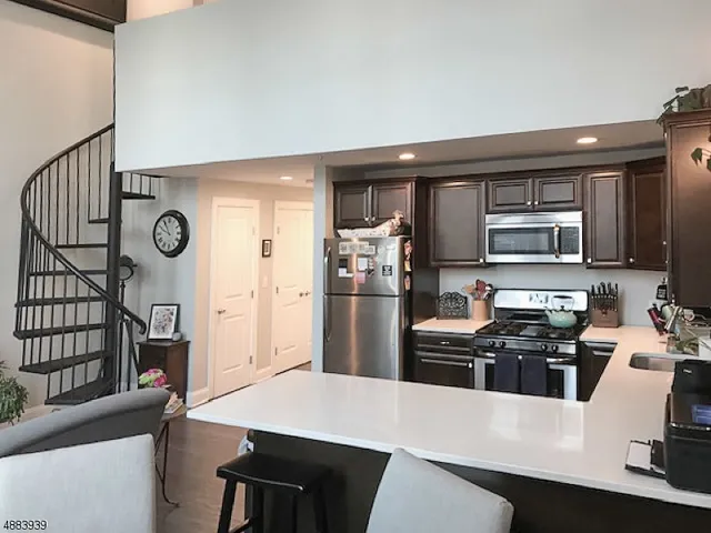 a kitchen with stainless steel appliances a refrigerator a stove a sink a dining table and chairs with wooden floor