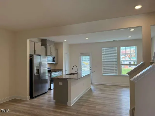 a kitchen with stainless steel appliances granite countertop a refrigerator a sink dishwasher and a oven with wooden floor