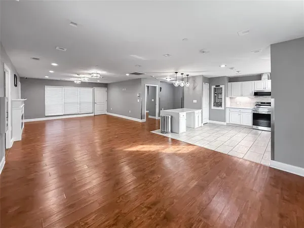 an empty room with wooden floor and kitchen view