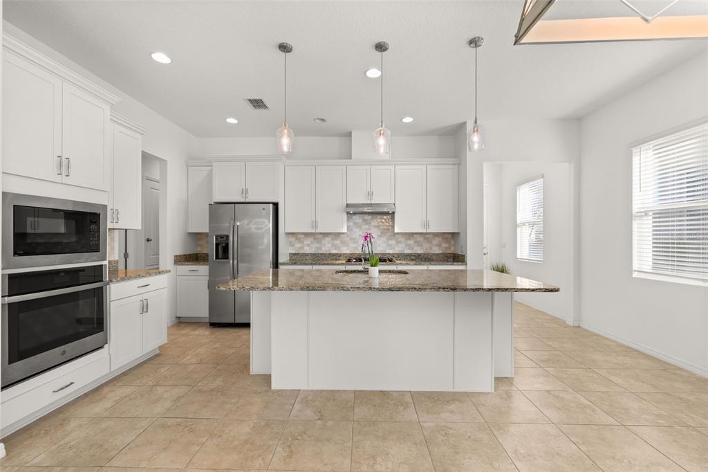 1855 Flora Pass Place Kissimmee, FL 34747 - Photo 24 of 41 a large kitchen with stainless steel appliances kitchen island granite countertop a stove a sink a refrigerator a center island a stove and a window