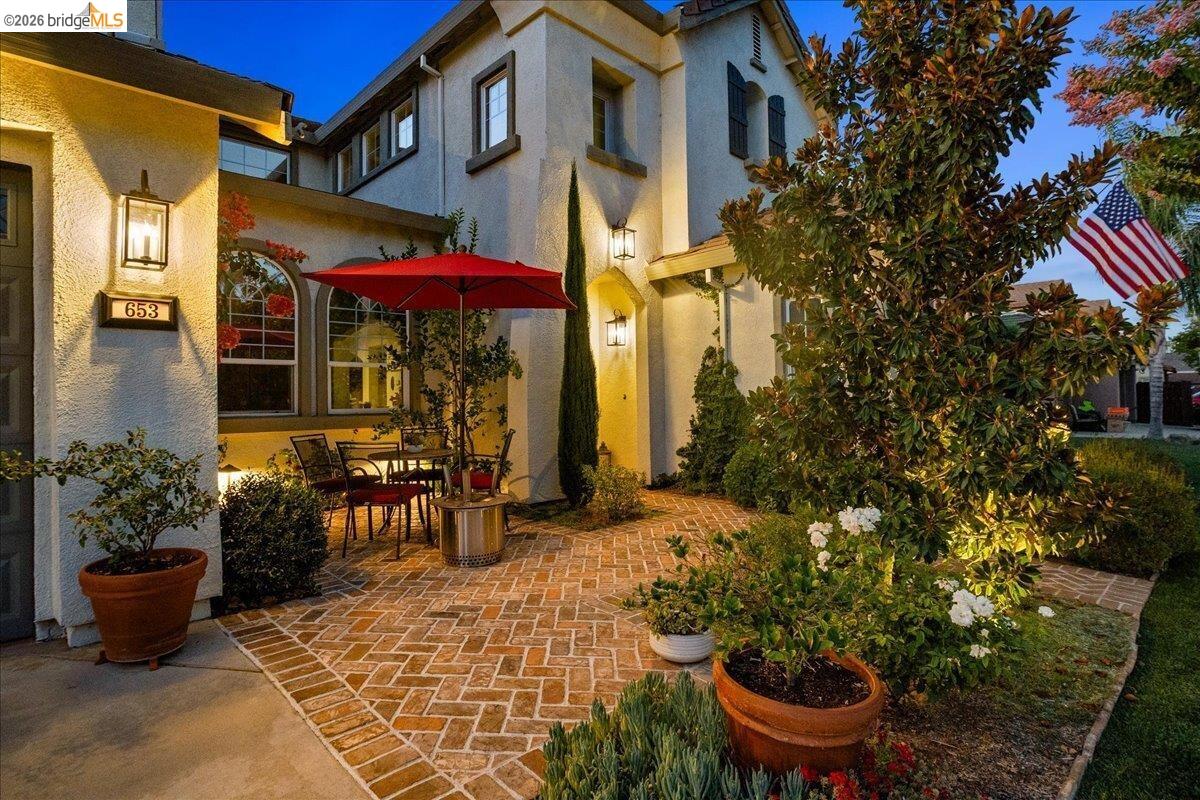 Stucco exterior with multiple windows, arched window accents, exterior lighting fixtures, and a brick paver patio
