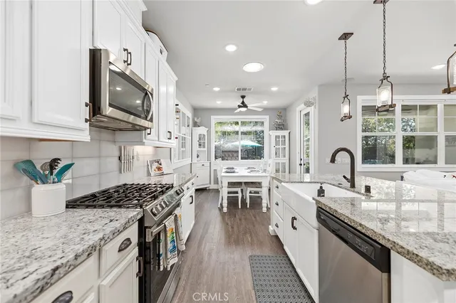 a large kitchen with stainless steel appliances kitchen island granite countertop a stove a sink dishwasher and white cabinets with wooden floor