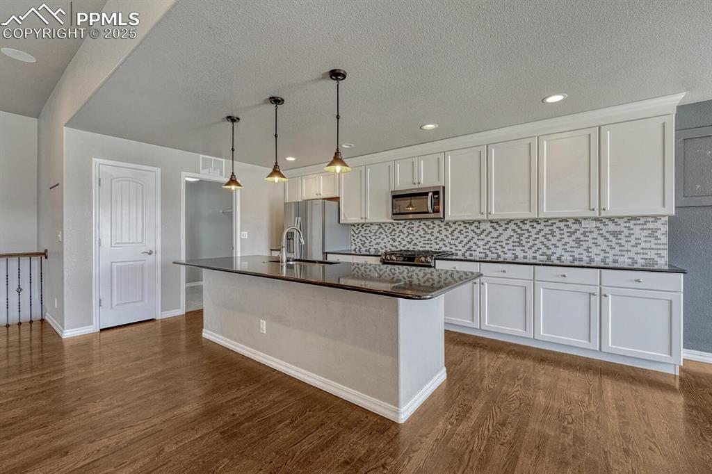 8437 Salt Brush Road Colorado Springs, CO 80908 - Photo 16 of 45 Bring your passion for cooking to life in this exceptional kitchen, boasting premium stainless steel appliances, elegant wood floors, a practical kitchen island with sink, sophisticated white cabinetry, and a stunning decorative backsplash that completes the look.