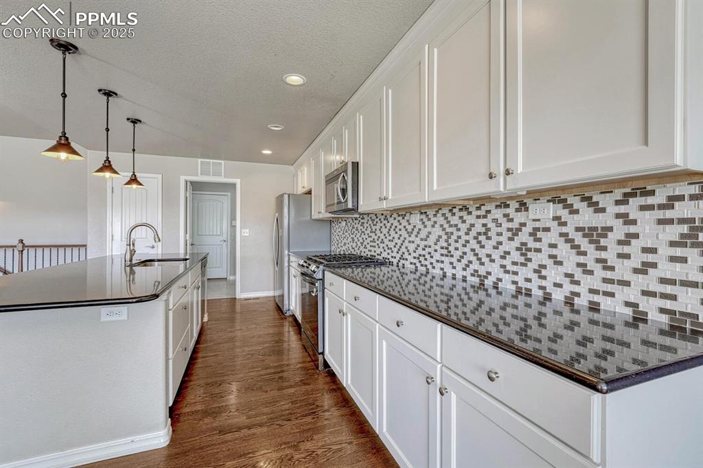8437 Salt Brush Road Colorado Springs, CO 80908 - Photo 17 of 45 Bring your passion for cooking to life in this exceptional kitchen, boasting premium stainless steel appliances, elegant wood floors, a practical kitchen island with sink, sophisticated white cabinetry, and a stunning decorative backsplash that completes the look.